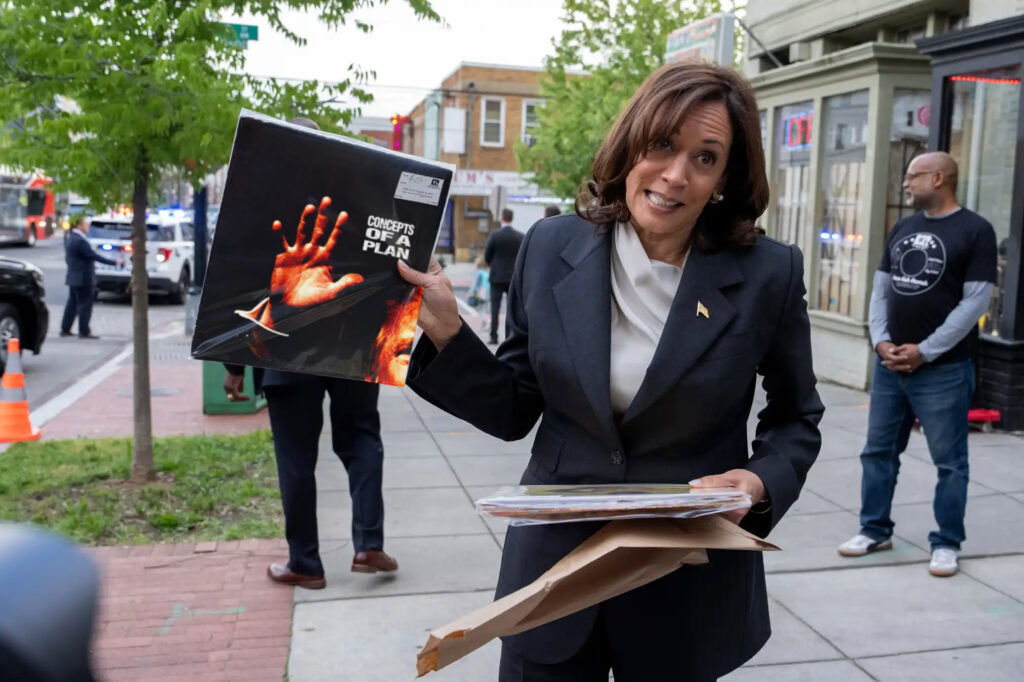 Kamala Harris holds up an album titled "Concepts of a Plan" with a cover that features an orange hand and a sliver of a terrible former president's face.