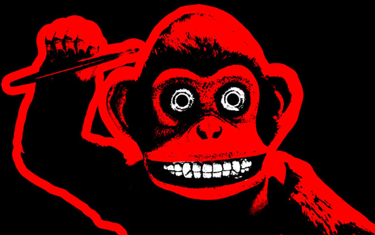 The titular monkey from The Monkey, shown in three tones. Black with red highlights, with white teeth and eyes. His right arm is raised and his right hand holds a drumstick. The background is solid black.